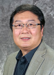 Zhang, Zhong-Yin 2017-03-08 www Headshot of Zhong-Yin Zhang in a blue shirt and gray blazer in front of a dark gray photo backdrop.