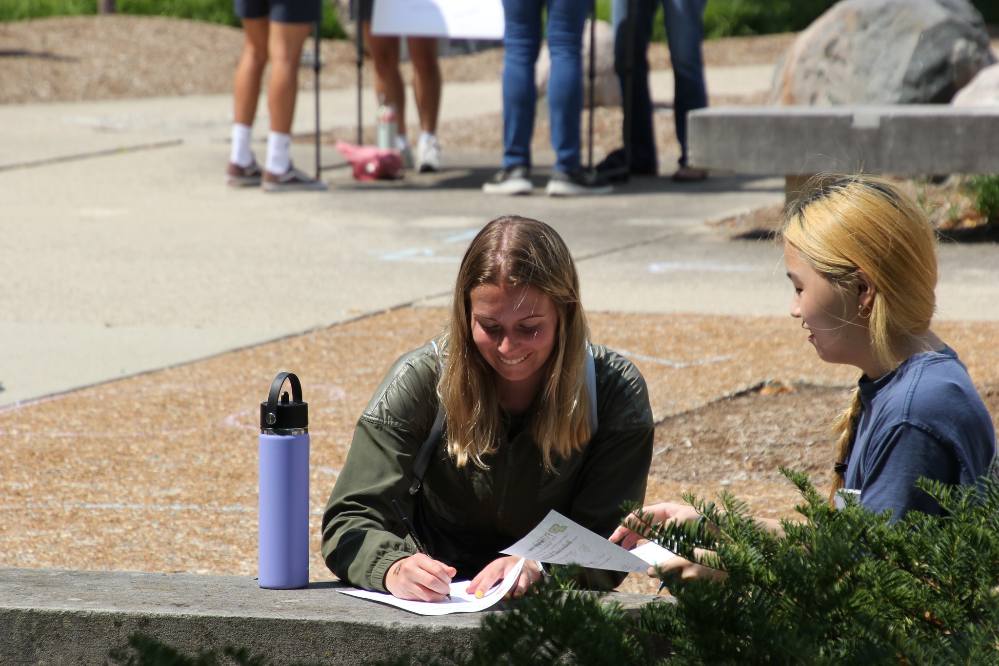 Two female students sit on a bench in the RHPH courtyard writing on a piece of paper.