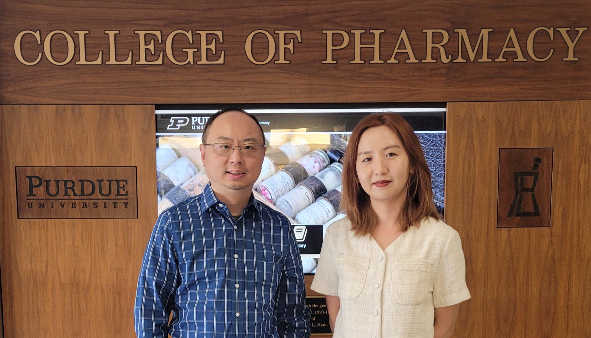 Tony Zhou and graduate student Yijing Huang stand in front of a wooden wall that reads