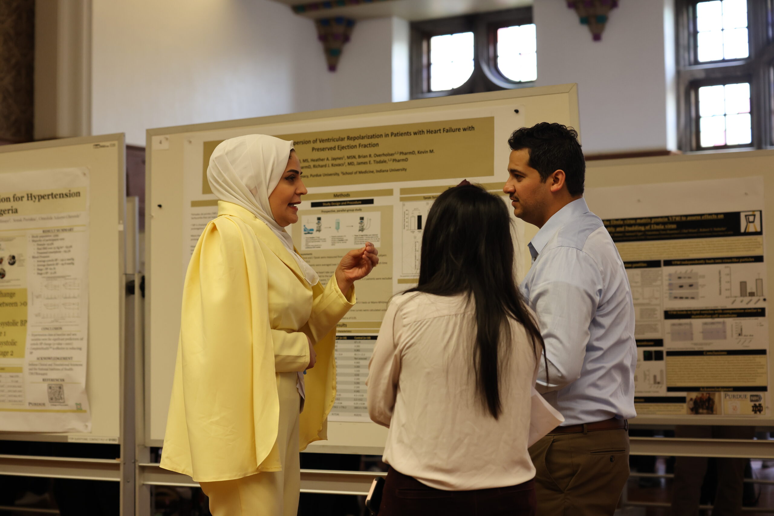 Two females and a male discuss research posters at Purdue Research Day.