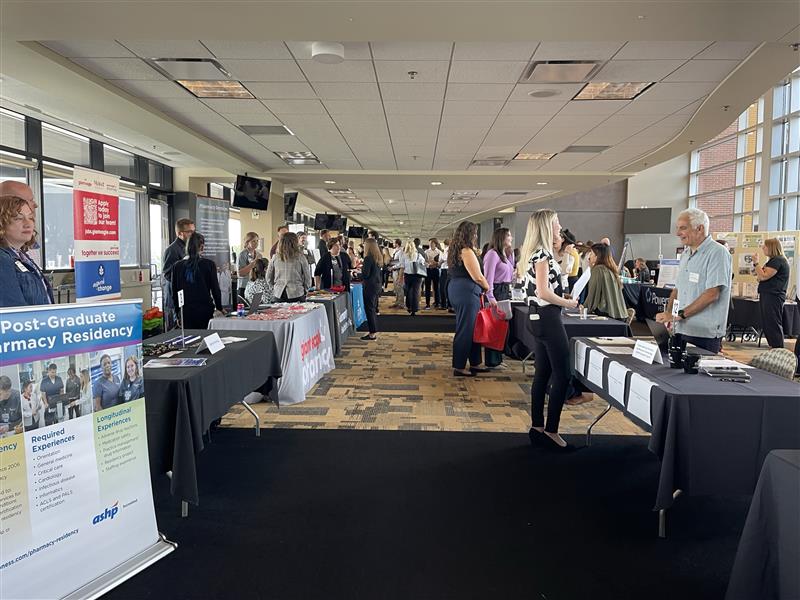 Wide-angled shot of people networking and visiting employer booths at a career fair.