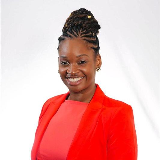 Omolola (Lola) Adeoye-Olatunde wearing an orange business suit in front of a white photo backdrop.