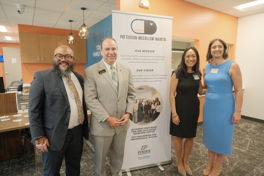 John Allen, Eric Barker, Jasmine Gonzalvo, and Brooke Patterson stand next to a sign unveiling Purdue's Patterson-McCallum-Maretta Charitable Pharmacy at Gleaners in Indianapolis.