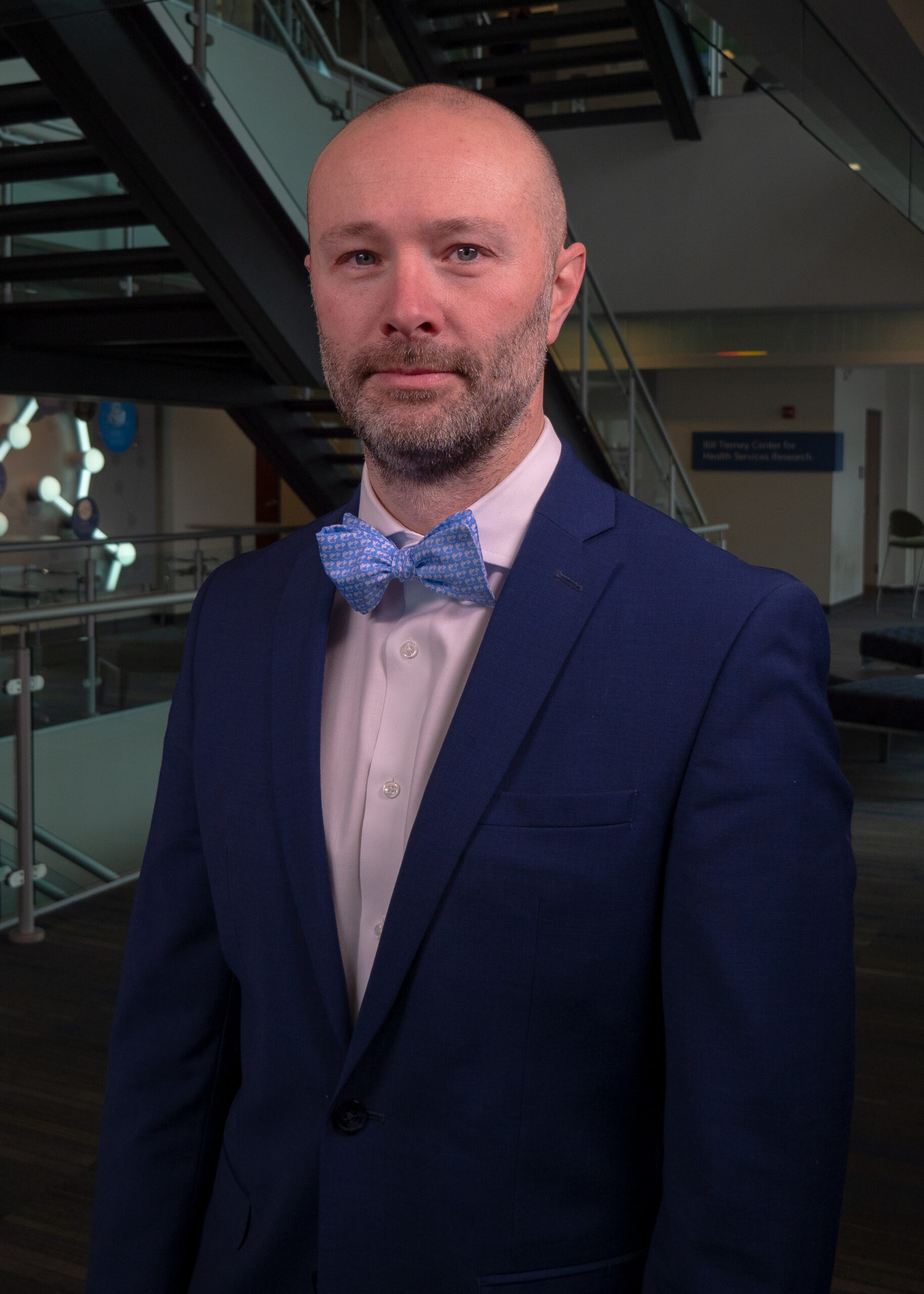 Headshot of Noll Campbell wearing a navy suit jacket, light button-up shirt, and medium blue bowtie.