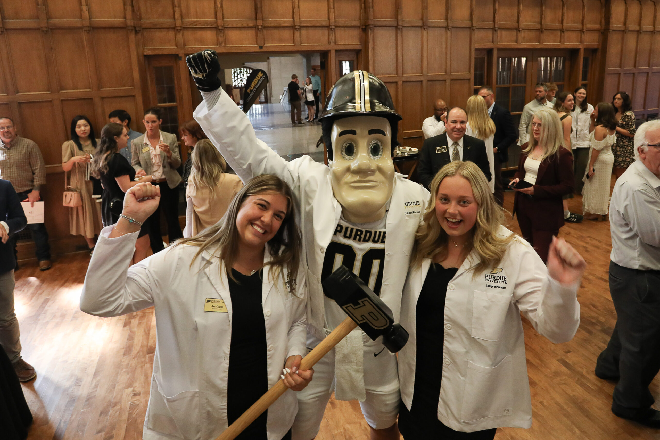 Two female pharmacy students stand on either side of Purdue Pete. All are wearing white coats.