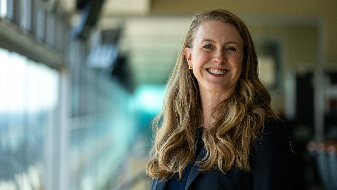 Careers Web Header Headshot of Stephanie Arnett smiling at the camera. The background is blurred windows with natural light in a football suite.