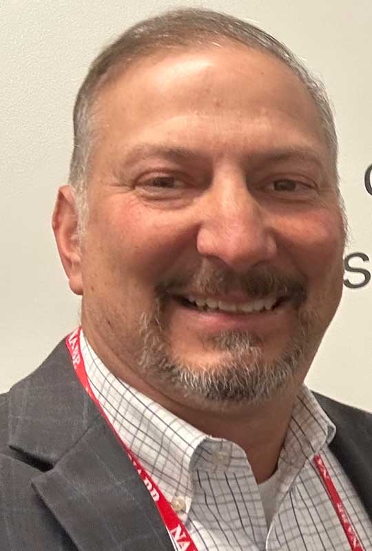 Headshot of Mark Bunton looking at the camera. He's wearing a white shirt with gray suit jacket. The background is an off-white blank wall.