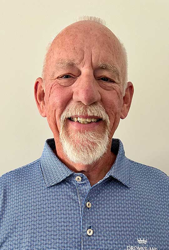 Headshot of Mike McNear wearing a medium blue dress shirt, smiling at the camera. The background is a white photo backdrop.