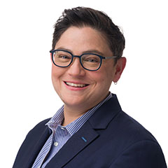 Headshot of Tara Lagu. She wears glasses, a blue blouse, and a navy blue blazer.