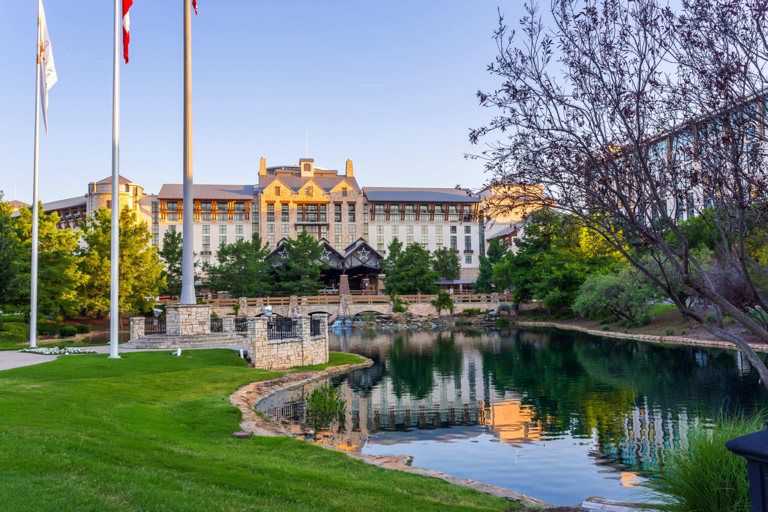Gaylord Texan Resort building and a flag view point in sunset in Grapevine, Dallas, Texas Landscape shot of the Gaylord Texan Resort and Convention center. The sky is blue and the resort reflects on a body of water surrounded by green grass.