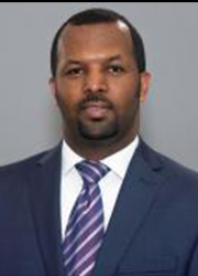 Headshot of Ephram Abebe. He is wearing a dark suit with white shirt and striped tie. The background is a gray photo backdrop.