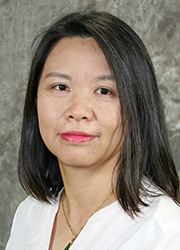 Headshot of Rong Huang. She wears a white dress shirt in front of a gray photo backdrop.