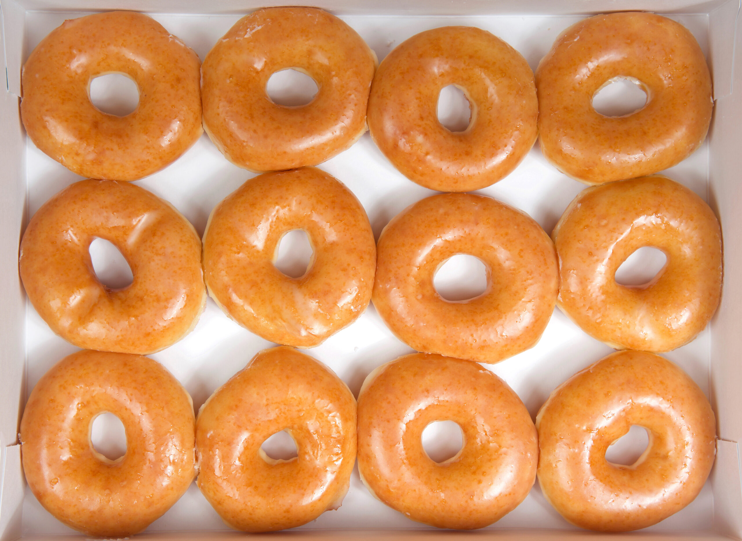 Overhead shot of 12 glazed donuts in a white donut box.