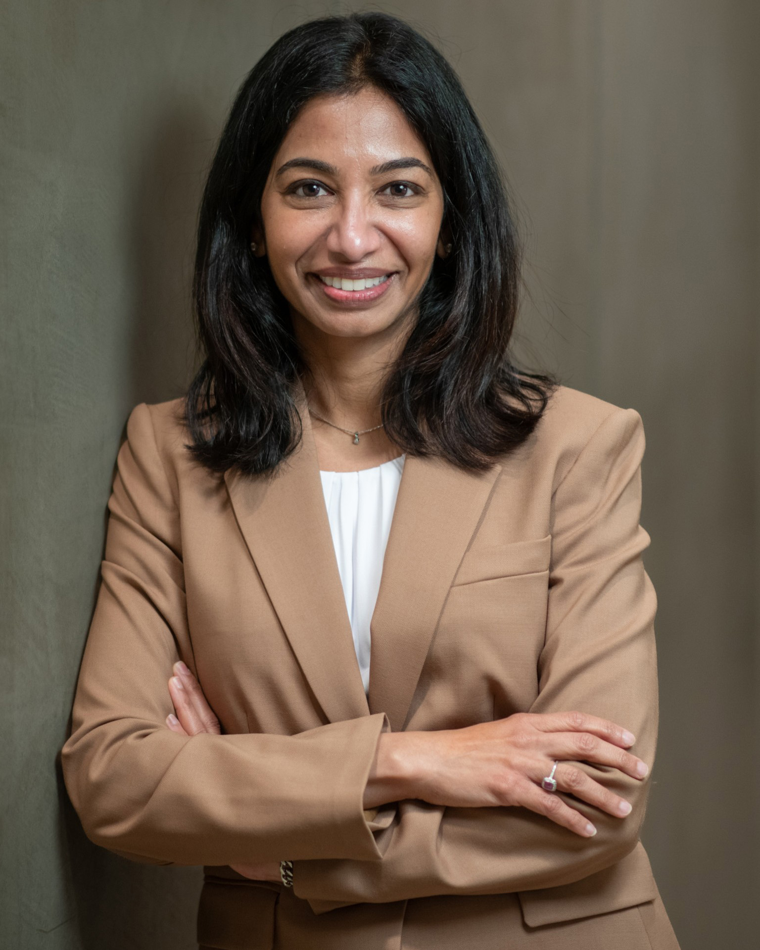 Headshot of Preeti Sivasankar in a tan suit in front of a gray backdrop.